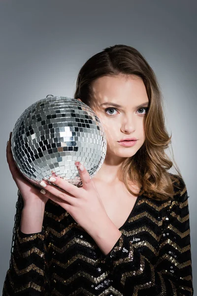 Mujer joven mirando a la cámara mientras sostiene la bola disco en gris - foto de stock