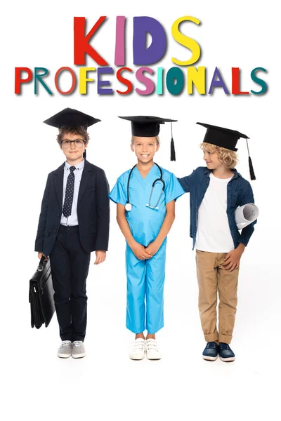 Children in graduation caps dressed in costumes of different professions standing near kids professionals lettering on white — Stock Photo