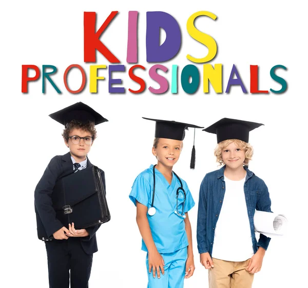 Children in graduation caps dressed in costumes of different professions near kids professionals lettering on white — Stock Photo