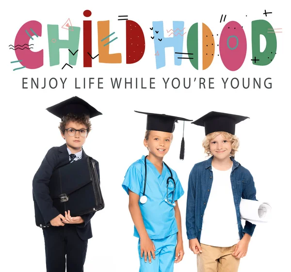 Kids in graduation caps dressed in costumes of different professions near childhood, enjoy life while you are young lettering on white — Stock Photo