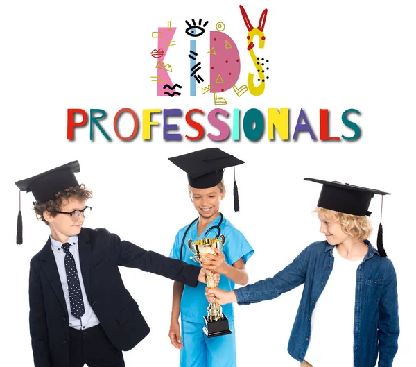 Jungen und Mädchen mit Abschlussmützen in Kostümen verschiedener Berufe halten goldene Trophäen in der Nähe von Kids Professionals Schriftzug auf weiß — Stockfoto