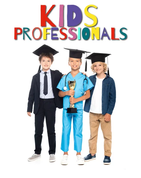 Kinder mit Abschlussmützen in Kostümen verschiedener Berufe halten goldene Trophäen in der Nähe von Kids Professionals Schriftzug auf weiß — Stockfoto