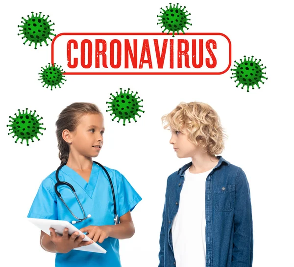 Kid in costume of doctor using digital tablet near curly boy and coronavirus lettering on white — Stock Photo