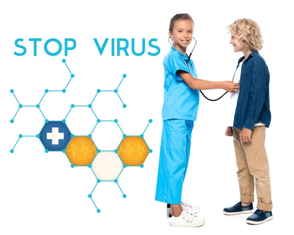 Criança em traje de médico examinando loira e menino encaracolado perto parar letras de vírus no branco — Fotografia de Stock