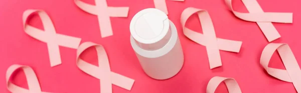 Tarro con pastillas cerca de cintas de conciencia de cáncer de mama borrosa sobre fondo rosa, pancarta - foto de stock