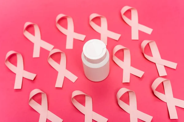 Jar with pills near ribbons of breast cancer awareness on blurred pink background — Stock Photo