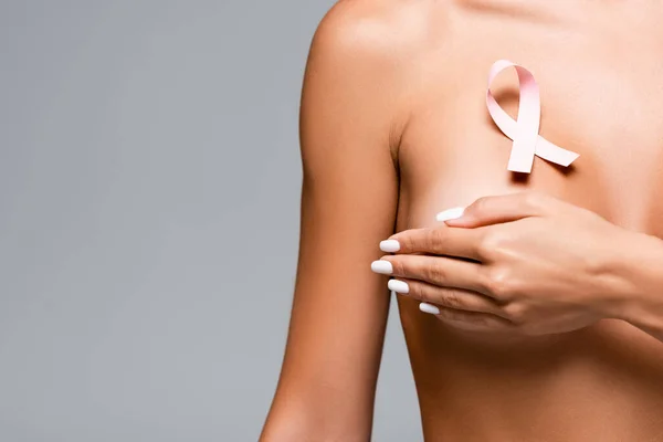 Vista recortada de la cinta rosa de la conciencia del cáncer de mama en el pecho de la mujer desnuda aislada en gris - foto de stock