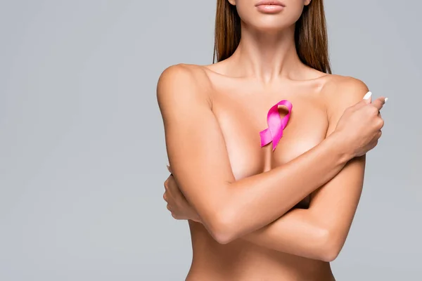 Vista recortada de mujer desnuda con cinta de conocimiento de cáncer de mama en busto aislado en gris - foto de stock