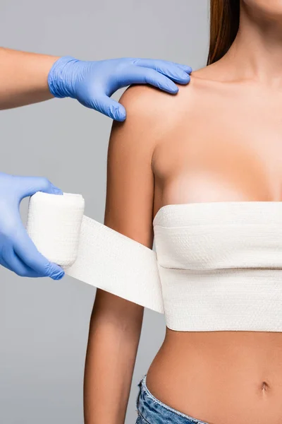 Vue recadrée du médecin enveloppant le sein d'une femme nue avec bandage élastique isolé sur gris — Photo de stock