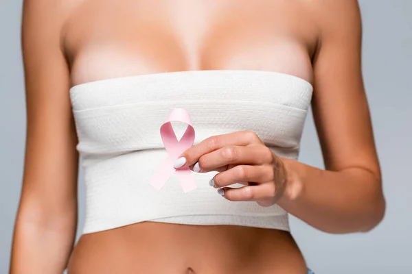 Vista ritagliata della donna con benda elastica sul seno che tiene il segno della consapevolezza del cancro al seno isolato su grigio — Foto stock