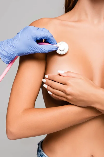 Обрізаний вид лікаря, який вивчає груди оголеної жінки зі стетоскопом ізольовано на сірому — стокове фото