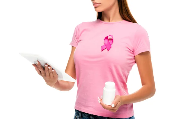 Vista ritagliata di giovane donna con nastro di consapevolezza del cancro al seno con tablet digitale e pillole isolate su bianco — Foto stock