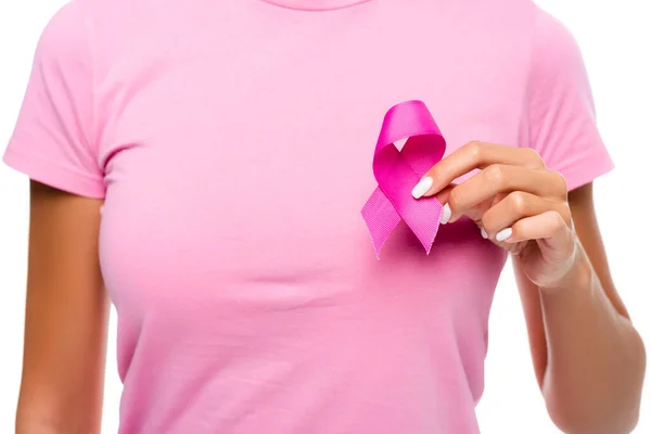Vista recortada de una mujer joven sosteniendo cinta de conciencia de cáncer de mama cerca del pecho aislado en blanco - foto de stock