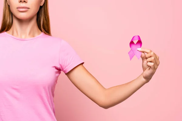 Vista recortada de una mujer joven que sostiene el símbolo de la conciencia del cáncer de mama aislado en rosa - foto de stock