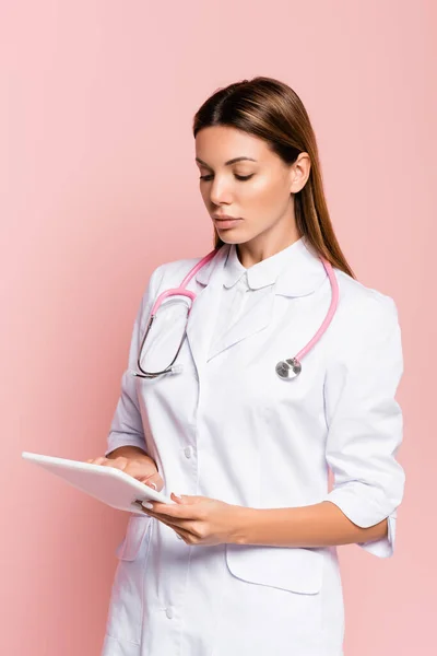 Доктор зі стетоскопом з використанням цифрового планшета ізольовано на рожевому — стокове фото