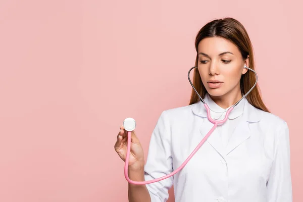 Brunette doctor in white coat holding stethoscope isolated on pink — Stock Photo