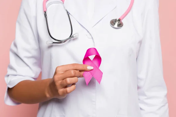 Vue recadrée du médecin en manteau blanc tenant un ruban rose de sensibilisation au cancer du sein isolé sur rose — Photo de stock