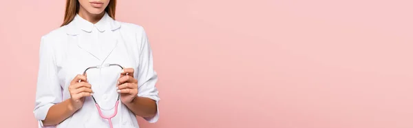 Vista cortada de médico morena segurando estetoscópio isolado em rosa, banner — Fotografia de Stock