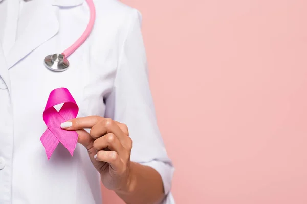 Vue recadrée du médecin tenant le symbole rose de la sensibilisation au cancer du sein isolé sur rose — Photo de stock