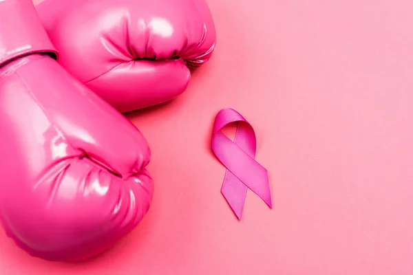 Vista superior de guantes de boxeo y cinta de conciencia de cáncer de mama en la superficie rosa - foto de stock