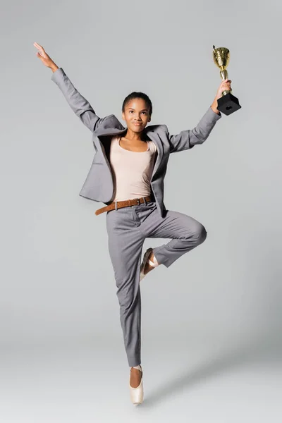 African american businesswoman performing ballet with golden cup isolated on grey — Stock Photo