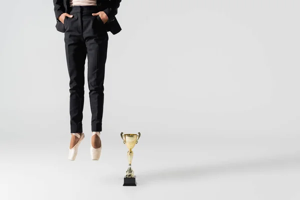 Cropped view of african american businesswoman in pointe shoes jumping near golden cup on grey — Stock Photo