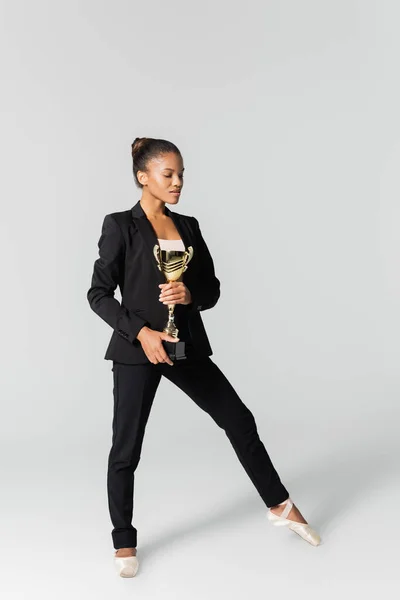 Афроамериканська бізнес-леді, що виконує балет із золотою чашкою ізольовано на сірому — стокове фото