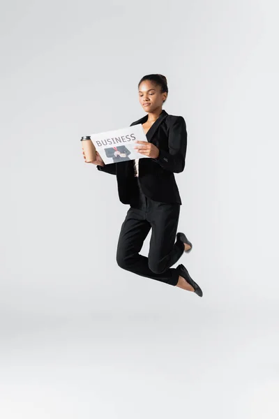 Femme d'affaires afro-américaine exécutant un ballet avec une tasse de journal et de papier isolé sur gris — Photo de stock