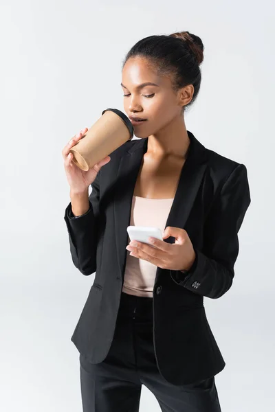 Афроамериканська бізнесменка з паперовою чашею за допомогою смартфона, ізольованого на сірому — стокове фото