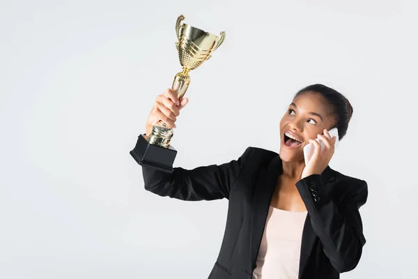 Happy african american businesswoman with golden cup talking on smartphone isolated on grey — Stock Photo