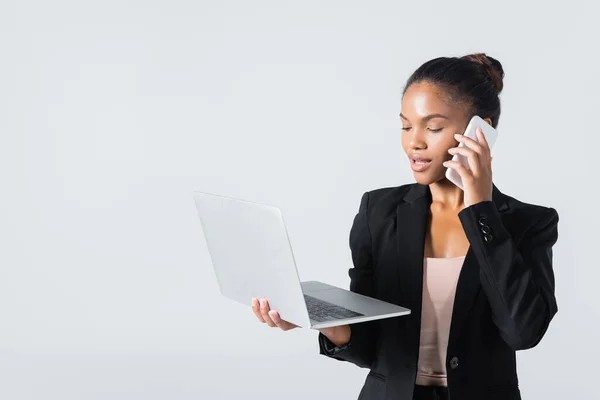 Femme d'affaires afro-américaine avec ordinateur portable parlant sur smartphone isolé sur gris — Photo de stock