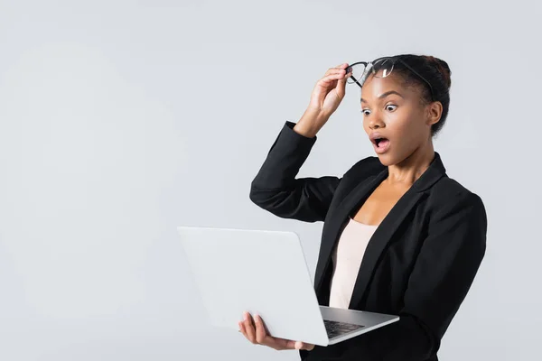 Шокована афроамериканська бізнес-леді в окулярах з ноутбуком ізольована на сірому — стокове фото