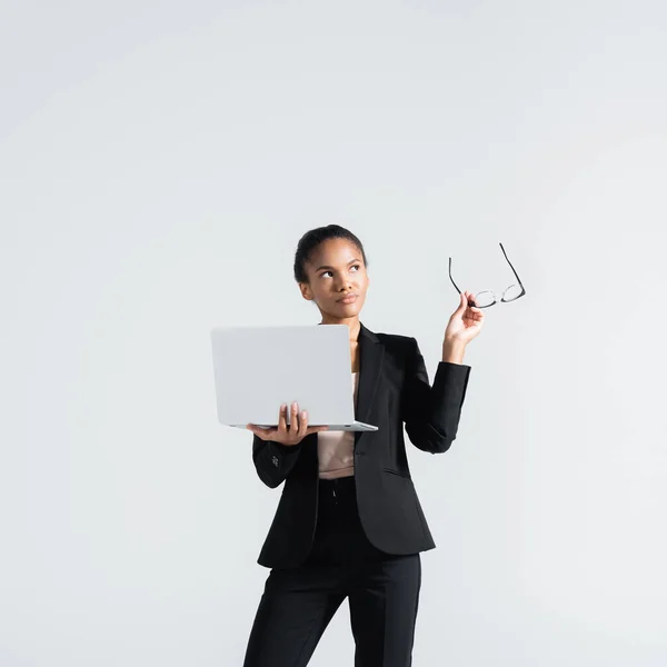 Donna d'affari africana americana pensierosa con occhiali e laptop isolato su grigio — Foto stock
