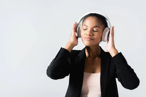 Femme d'affaires afro-américaine écoutant de la musique dans des écouteurs isolés sur gris — Photo de stock