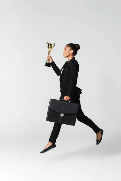 Side view of african american businesswoman with suitcase and goblet isolated on white — Stock Photo