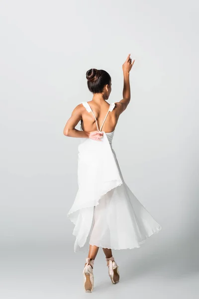 Back view of graceful african american ballerina in dress dancing on white background — Stock Photo