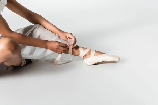 Vista recortada de la elegante bailarina afroamericana ajustando zapatos puntiagudos sobre fondo blanco - foto de stock