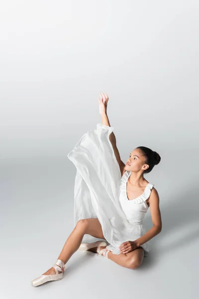 Витончена афроамериканська балерина в сукні танцює на підлозі на білому тлі — стокове фото