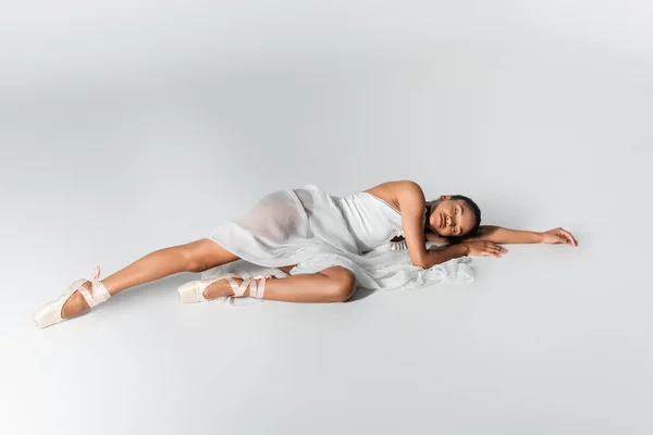 Graceful african american ballerina in dress lying on floor on white background — Stock Photo