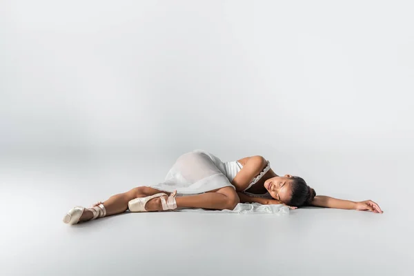 Graceful african american ballerina in dress lying on floor on white background — Stock Photo