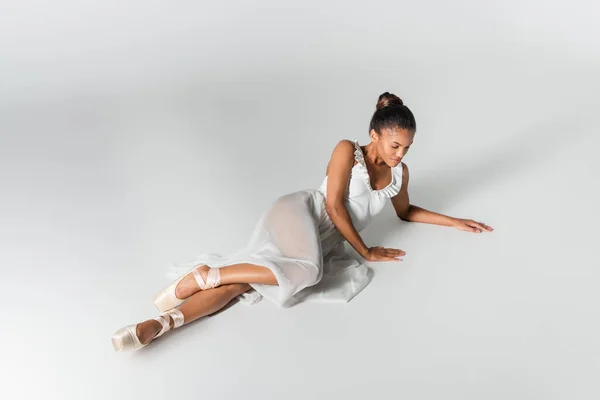 Изящная африканская балерина в платье, лежащая на полу на белом фоне — стоковое фото