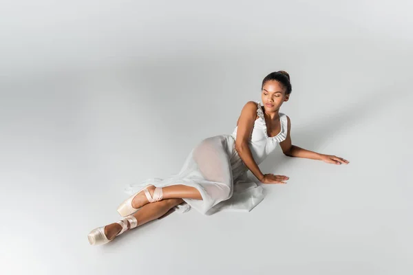 Graceful african american ballerina in dress lying on floor on white background — Stock Photo
