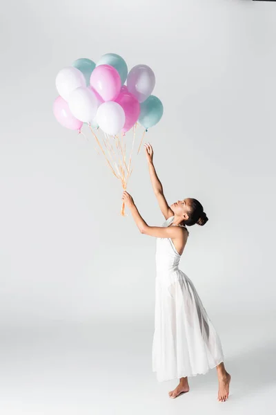 Descalza elegante bailarina afroamericana en vestido con globos sobre fondo blanco - foto de stock
