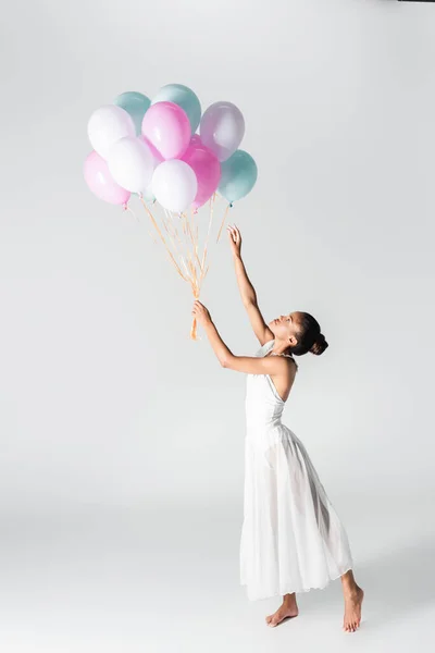 Barefoot graceful african american ballerina in dress with balloons on white background — Stock Photo