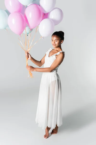 A piedi nudi graziosa ballerina afroamericana in abito con palloncini su sfondo bianco — Foto stock