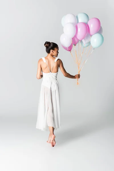 Vista posterior de descalzo elegante bailarina afroamericana en vestido con globos sobre fondo blanco - foto de stock