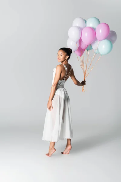 Barfuß anmutige afrikanisch-amerikanische Ballerina im Kleid mit Luftballons auf weißem Hintergrund — Stockfoto