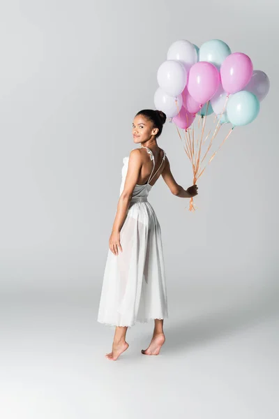 Descalza elegante bailarina afroamericana en vestido con globos sobre fondo blanco - foto de stock