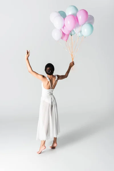 Босоніж витончена афроамериканська балерина в сукні танцює з повітряними кулями на білому тлі — Stock Photo