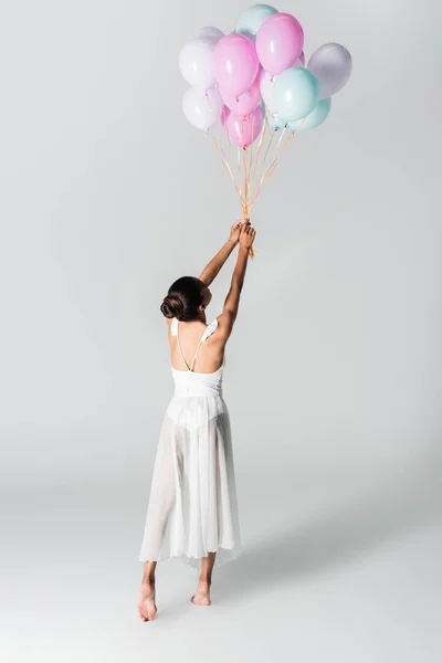 Atrás vista de descalzo elegante bailarina afroamericana en vestido bailando con globos sobre fondo blanco — Stock Photo